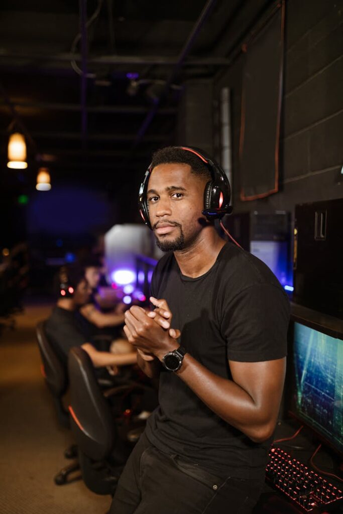A serious gamer wearing black headphones and a shirt, standing in a modern esports venue.